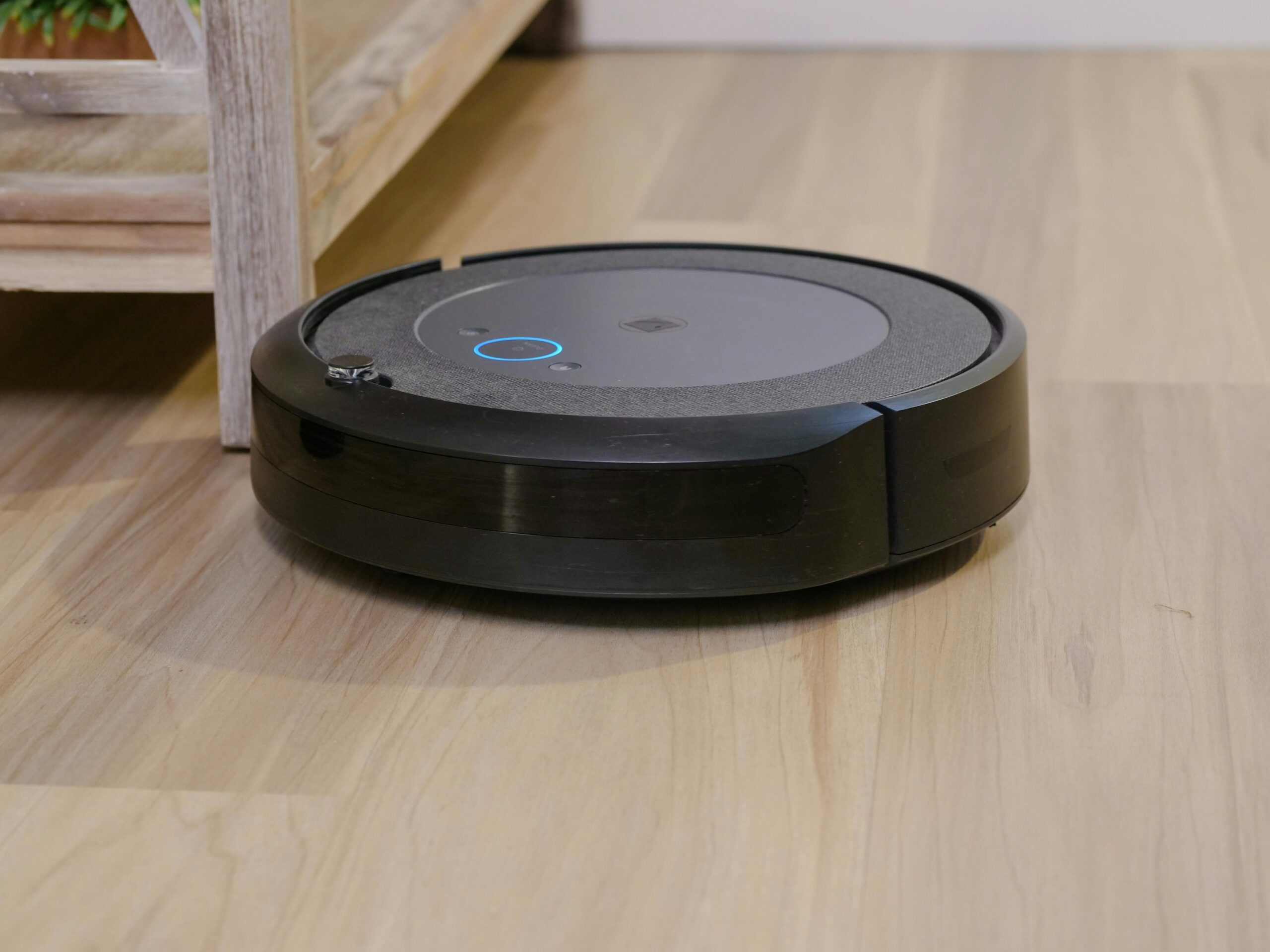 Autonomous vacuum cleaner navigating wooden floor indoors, showcasing smart home technology.