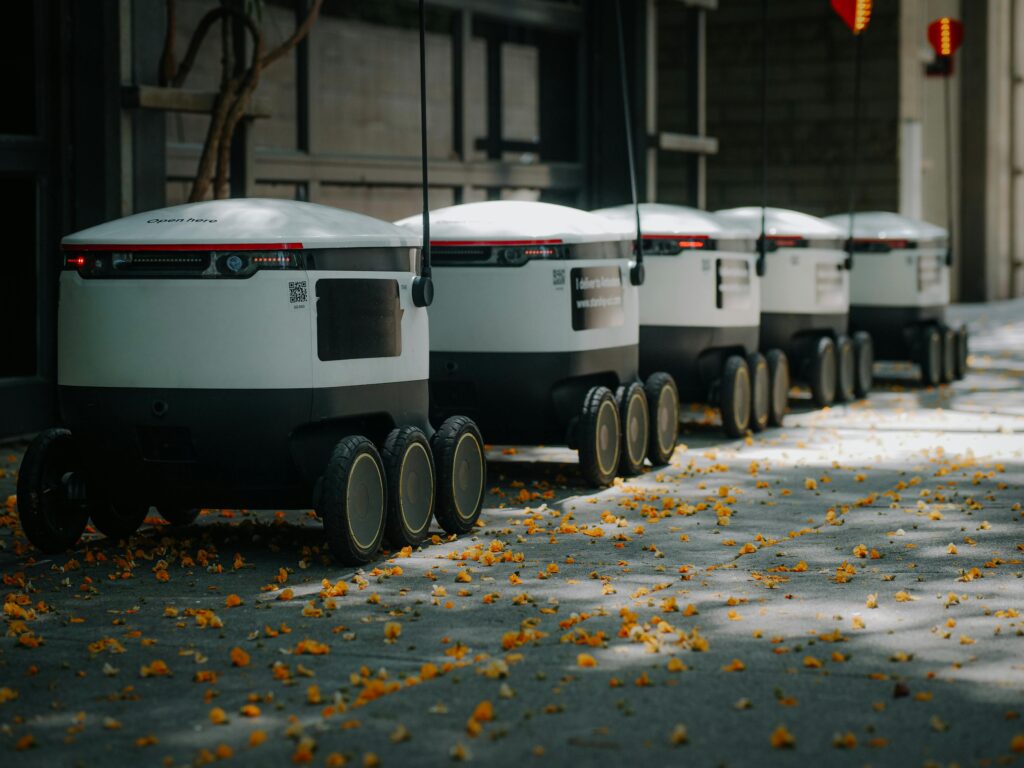 pexels-photo-8566636-8566636 Futuristic delivery robots lined up outdoors, showcasing innovative modern technology.